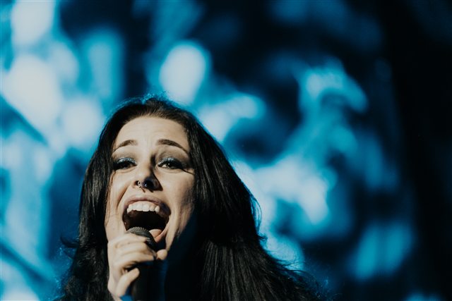Sarah singing into a microphone under blue stage lights
