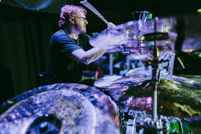 The drummer performing under blue and purple lights