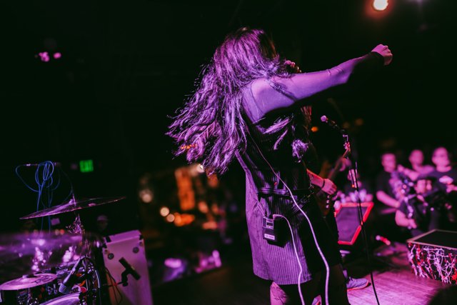 Sarah reaching toward the crowd under purple lights
