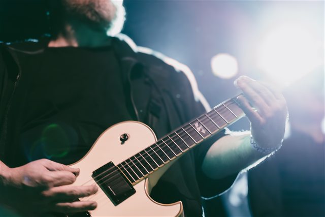 A close view of a guitar being played beneath stage lights