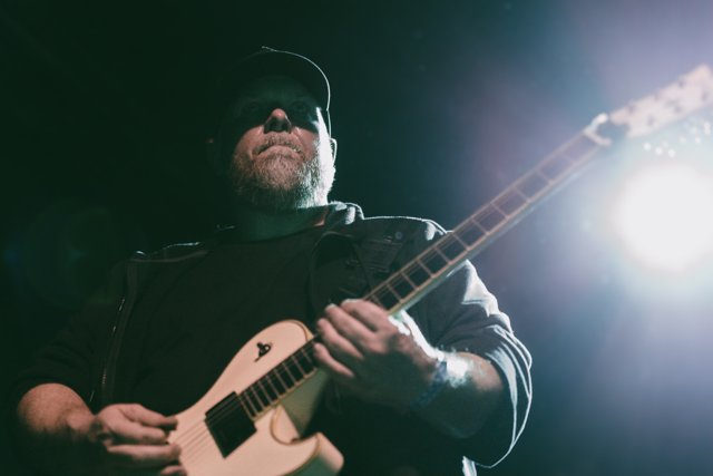 A guitarist playing a white guitar through stage haze