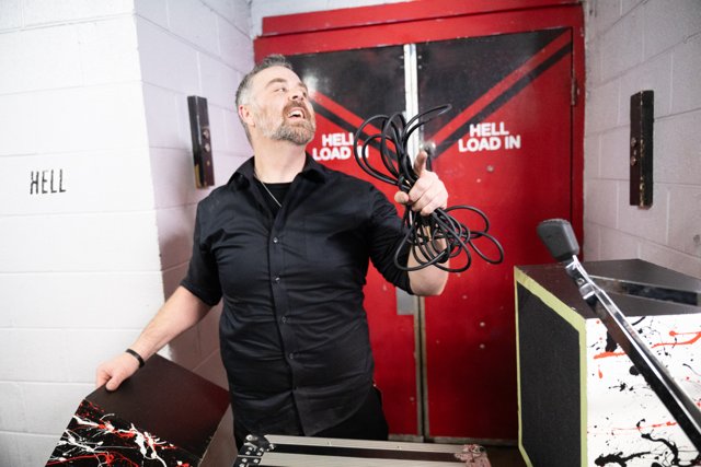 A band member holding gear beside a backstage door