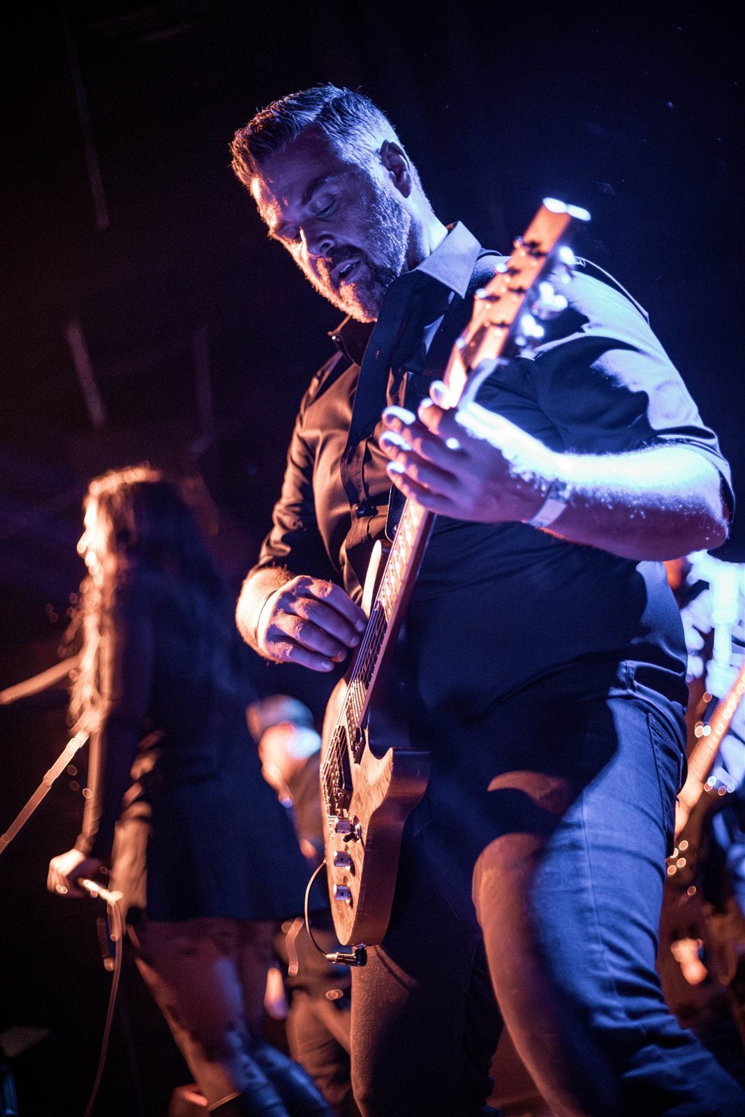 A guitarist leaning into the performance under blue and amber light