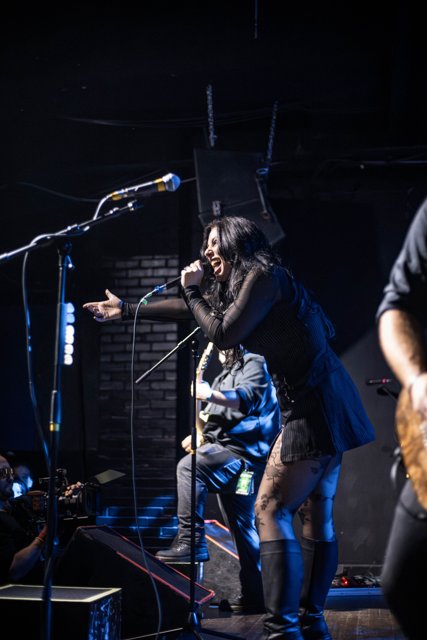 A guitarist singing into a microphone under blue lights