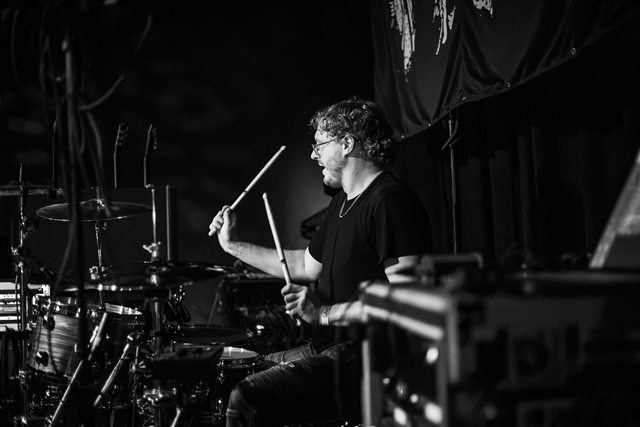 The drummer behind the kit in black and white