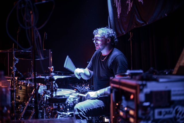 The drummer playing beneath purple lights