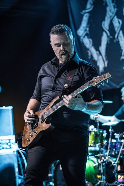 A guitarist concentrating on his instrument under blue lights