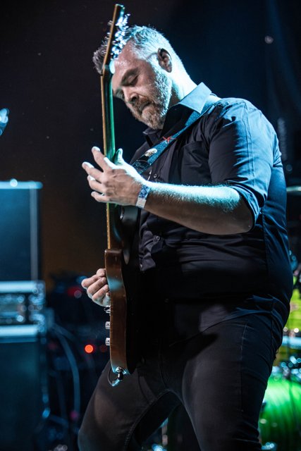 A guitarist singing and playing beneath blue lights