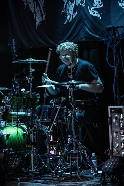The drummer playing under blue stage lights