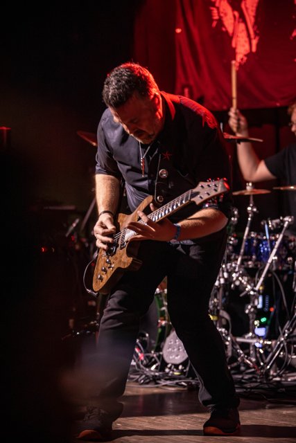 A guitarist performing beneath red lights