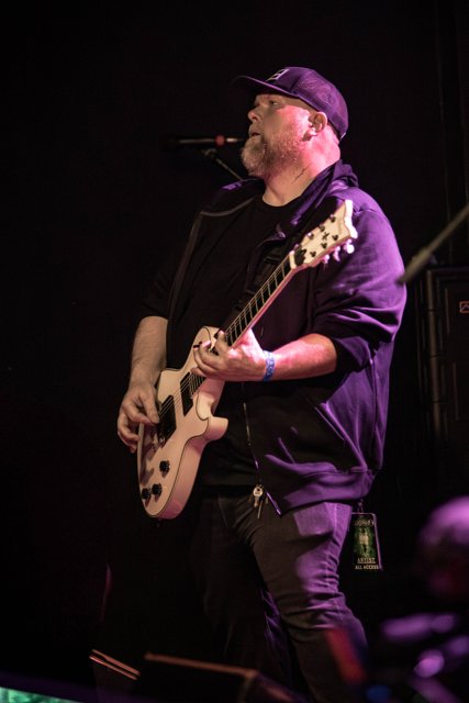 A guitarist playing beneath purple stage lights