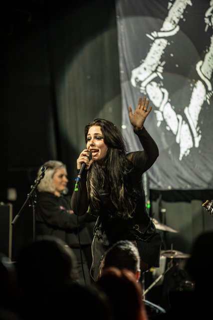 Sarah raising an arm beneath white stage lights