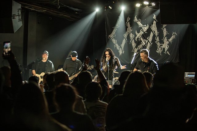 The audience facing Perrish 9 beneath white stage lights