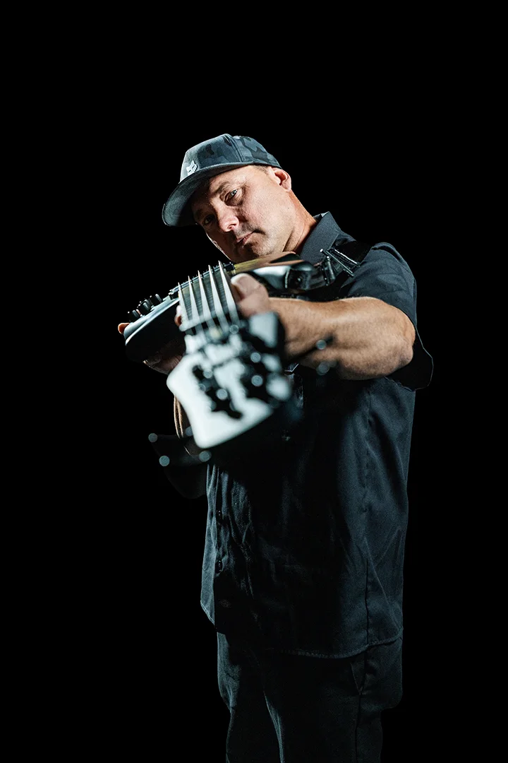 Bryan Poss holding a bass guitar against a black background