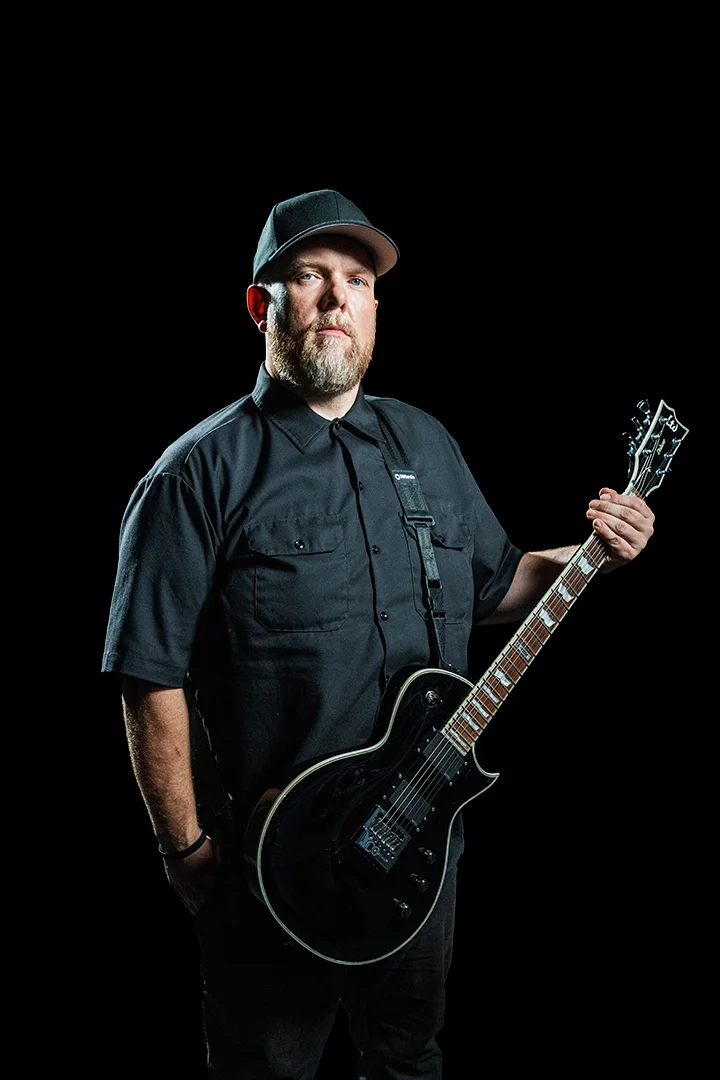 Matt Bryant holding a black guitar against a black background